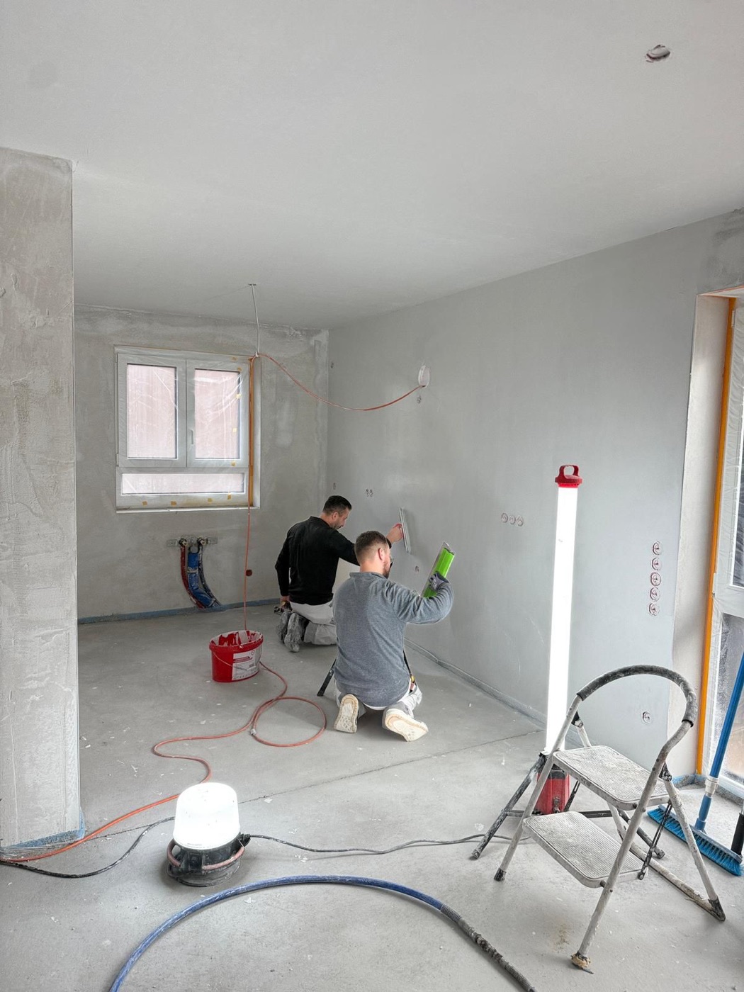 Zwei Mitarbeiter arbeiten kniend an den Wänden eines Rohbauzimmers