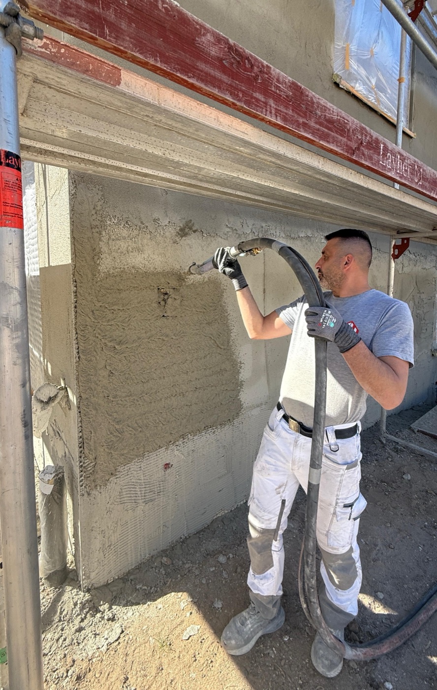 Mitarbeiter spritzt auf dem Gerüst Putz an eine Fassade