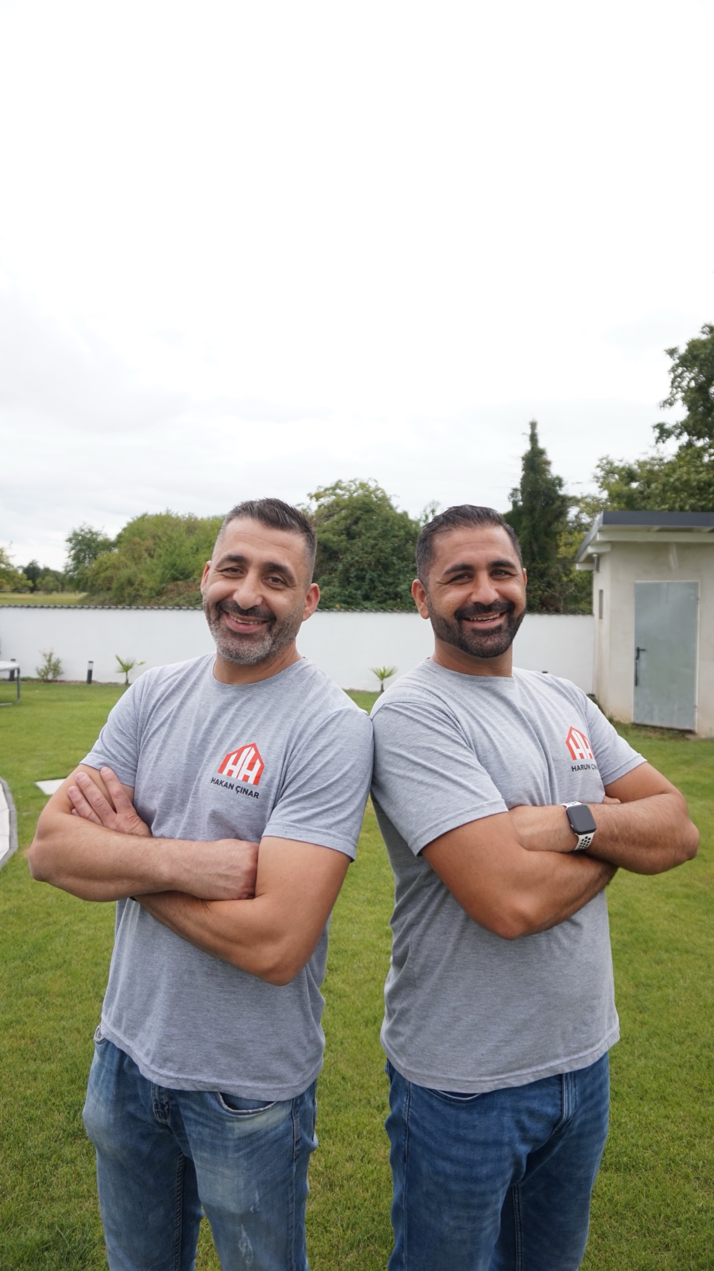 Harun und Hakan Cinar stehen Rücken an Rücken in ihren Arbeitsshirts