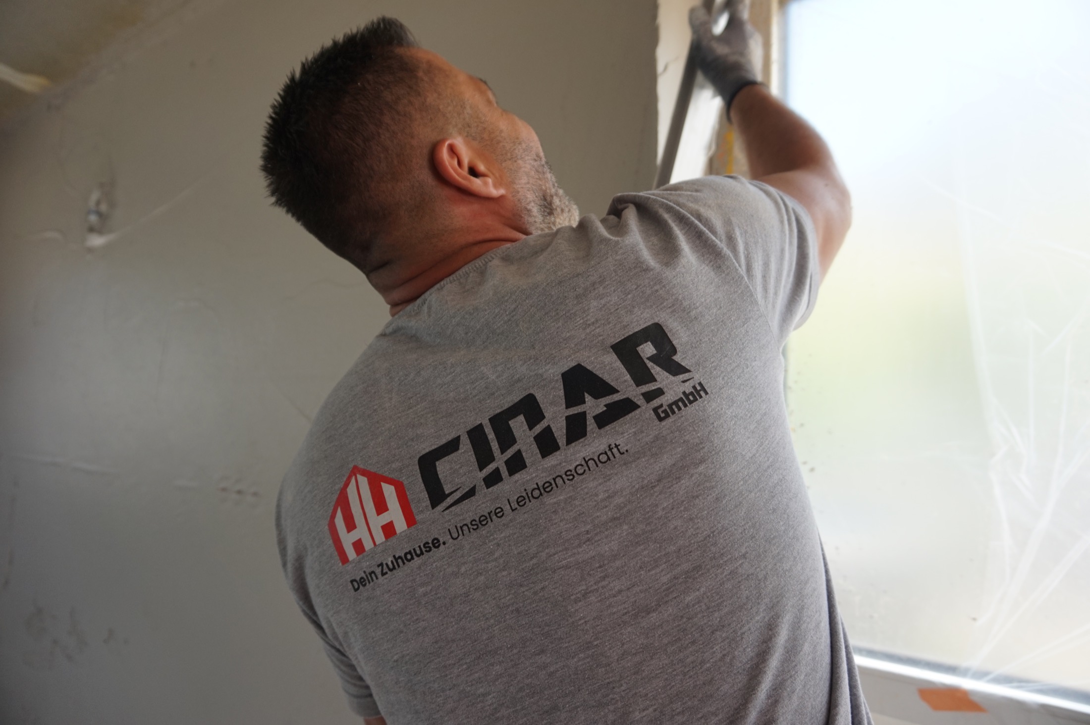 Hakan Cinar verputzt eine Wand, auf dem Rücken seines Shirts das HH-Cinar-Logo