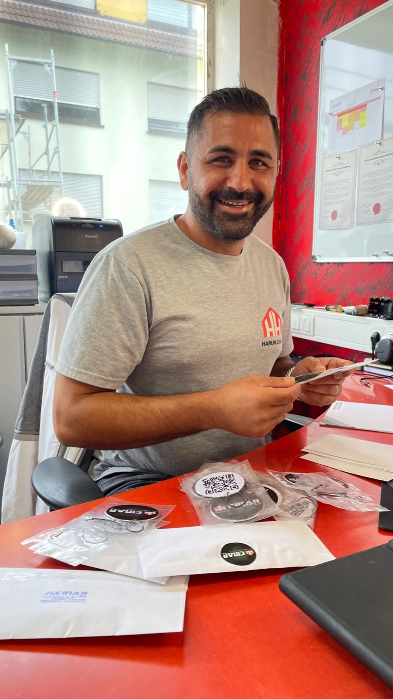 Harun Cinar sitzt lächelnd im Büro und bereitet HH-Cinar-Sticker vor