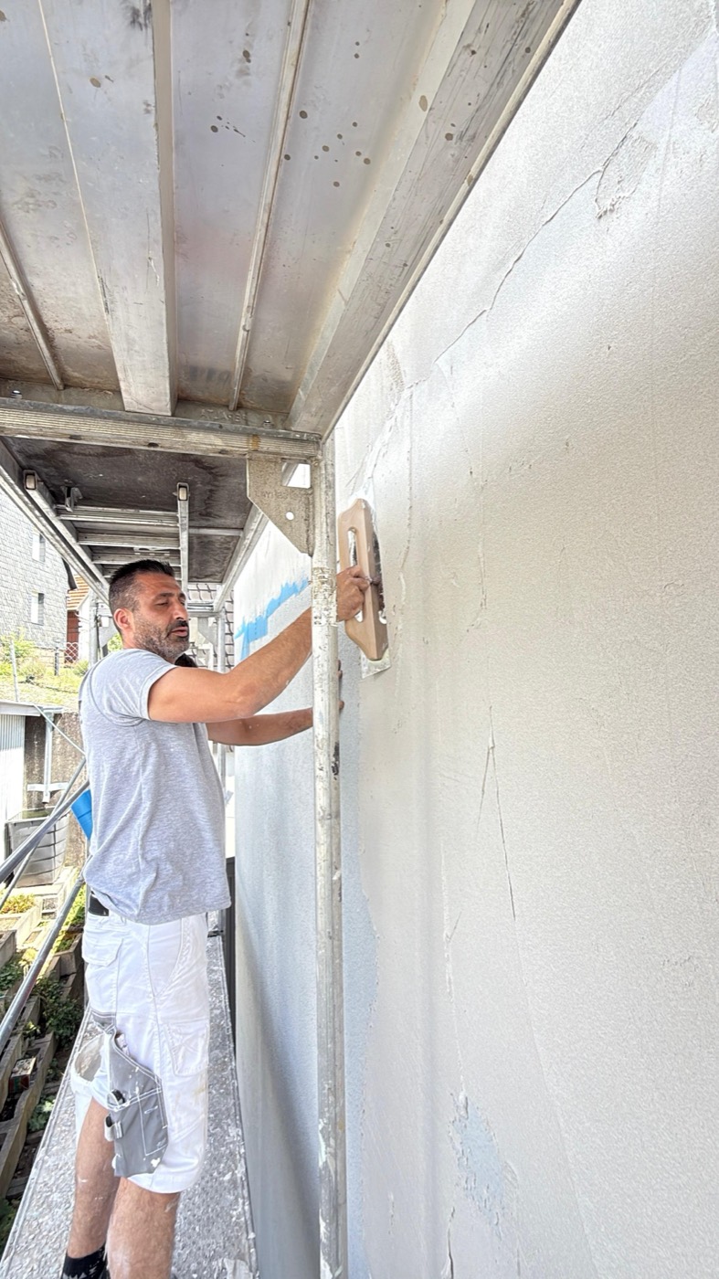 Mitarbeiter verputzt auf einem Gerüst eine Außenwand