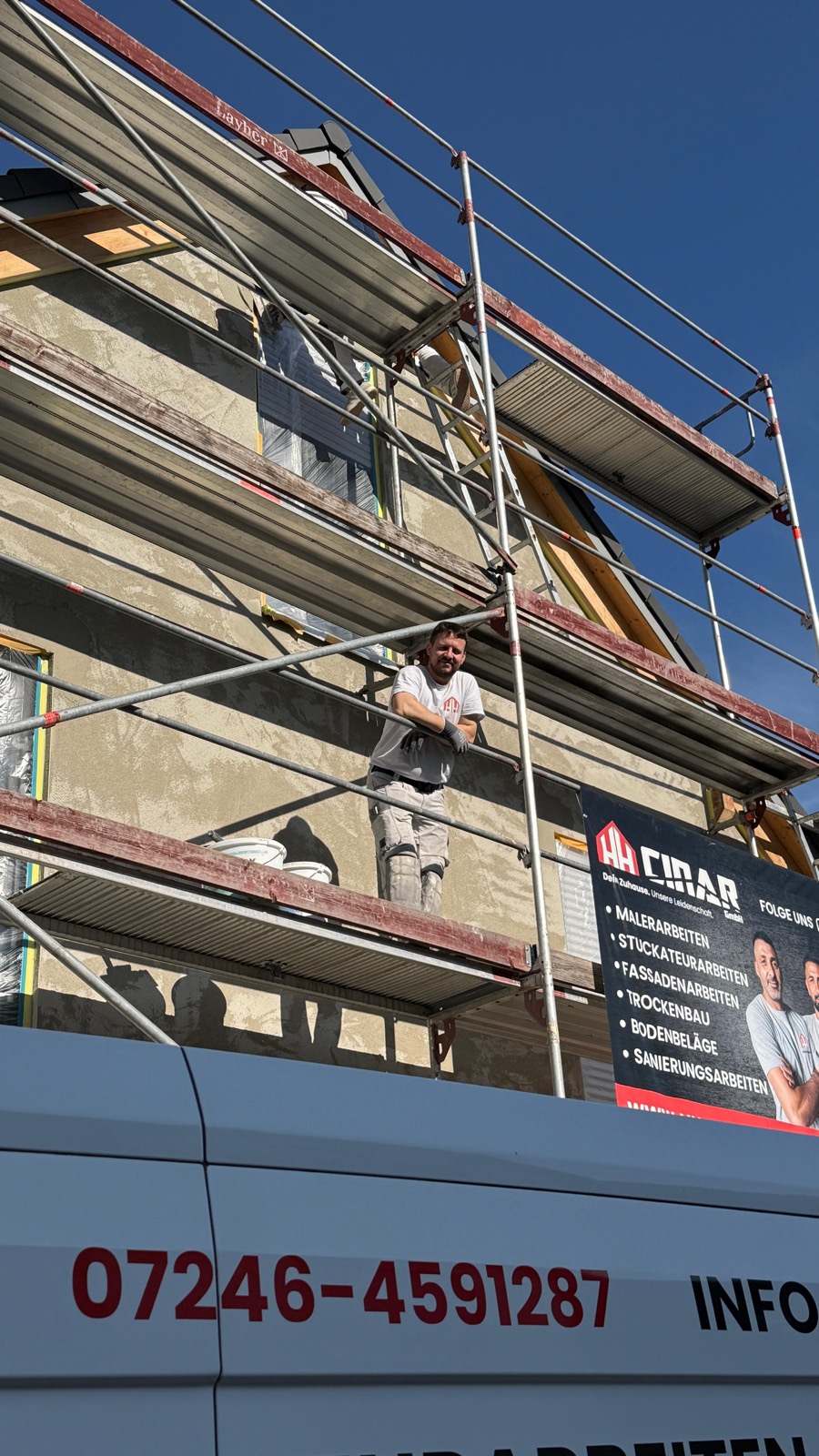 Mitarbeiter steht auf einem Gerüst vor einer Fassade, davor der HH-Cinar-Transporter