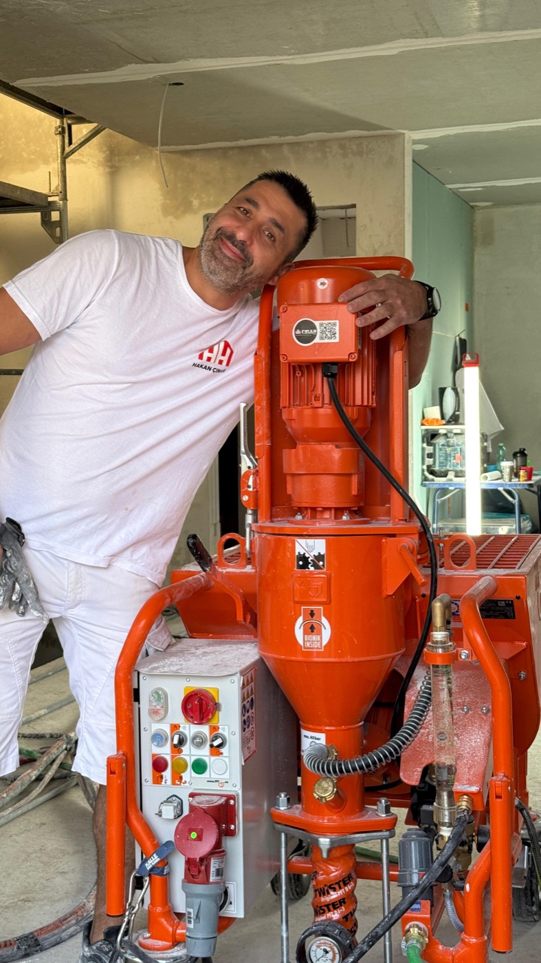 Mitarbeiter lehnt lächelnd an einer modernen Putzmaschine auf der Baustelle