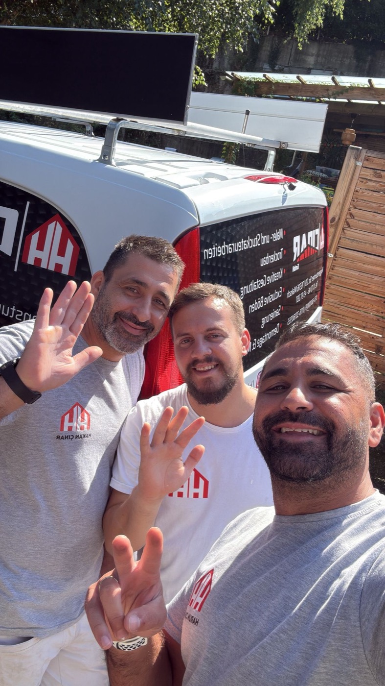 Drei Mitglieder des HH-Cinar-Teams winken vor dem Firmentransporter in die Kamera